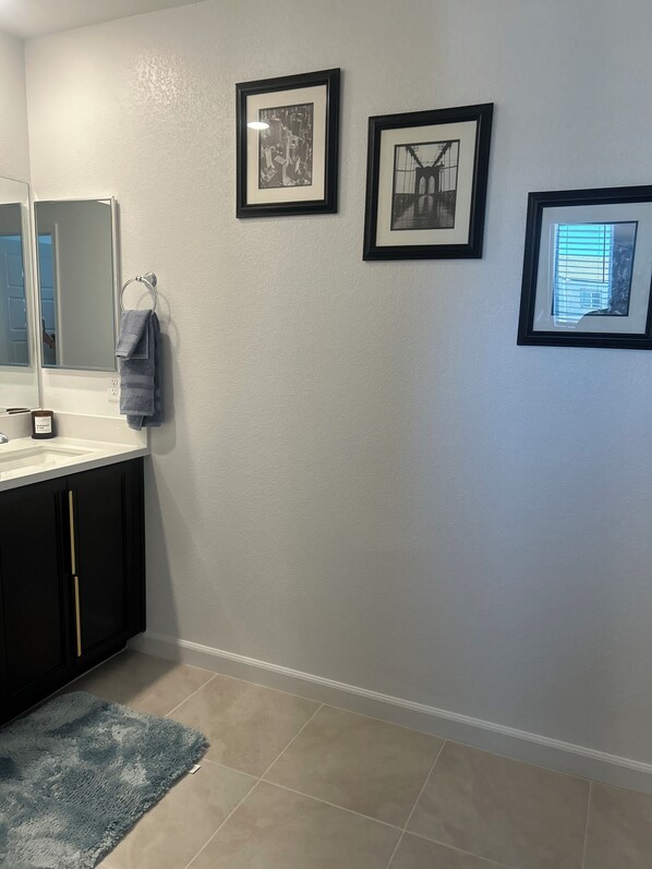 A bathroom with a white wall, a sink with a mirror, and three framed pictures.
