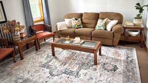 A living room with a brown sofa, a glass coffee table, a red chair, a wooden side table, and a patterned rug.