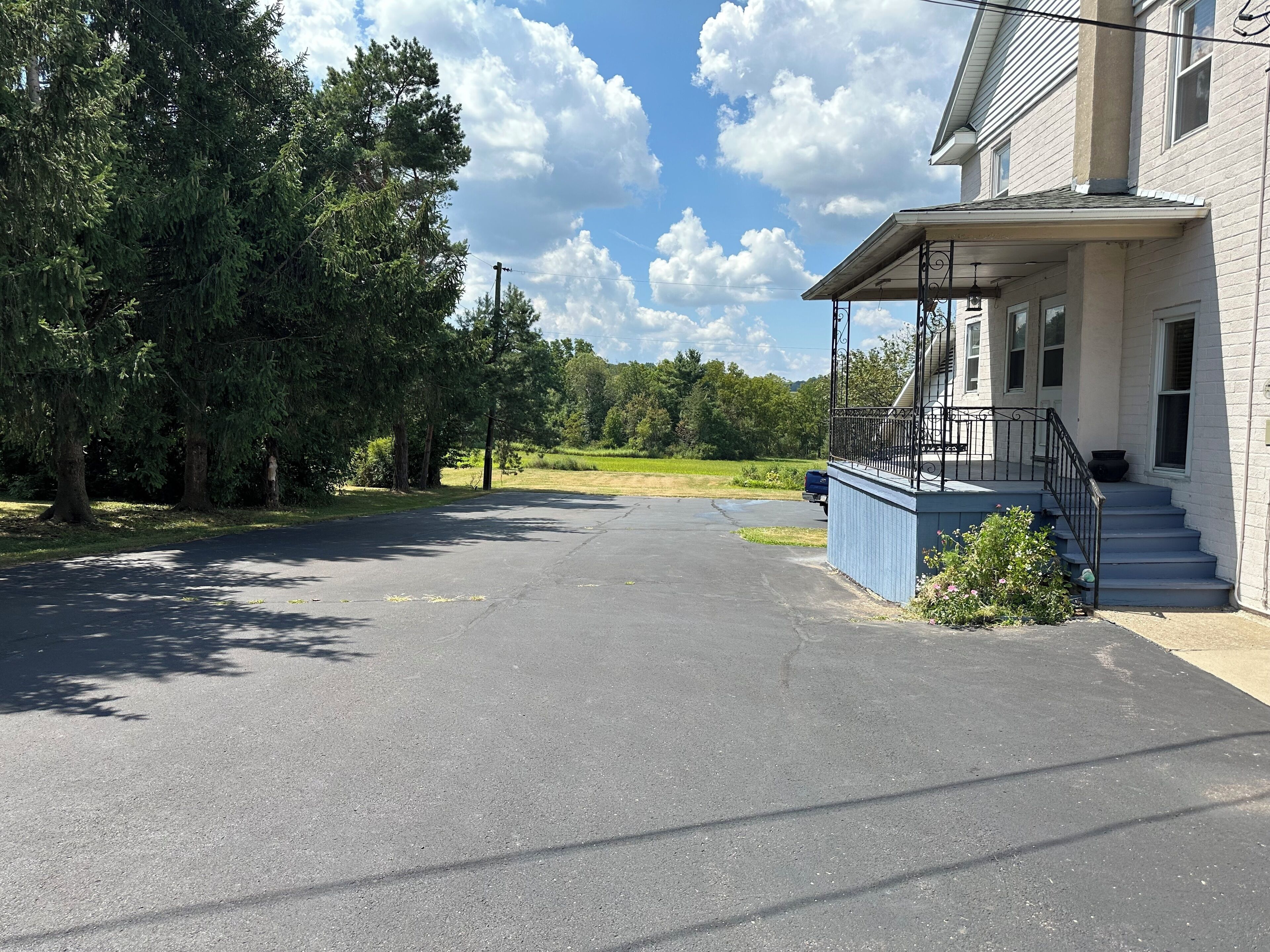 A building with a covered porch and a driveway leading to a parking area.