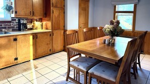 A kitchen with wooden cabinets, a dining table with chairs, and a window with blinds.