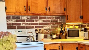A kitchen with wooden cabinets, a brick backsplash, a stove, a microwave, and a dining table with chairs.
