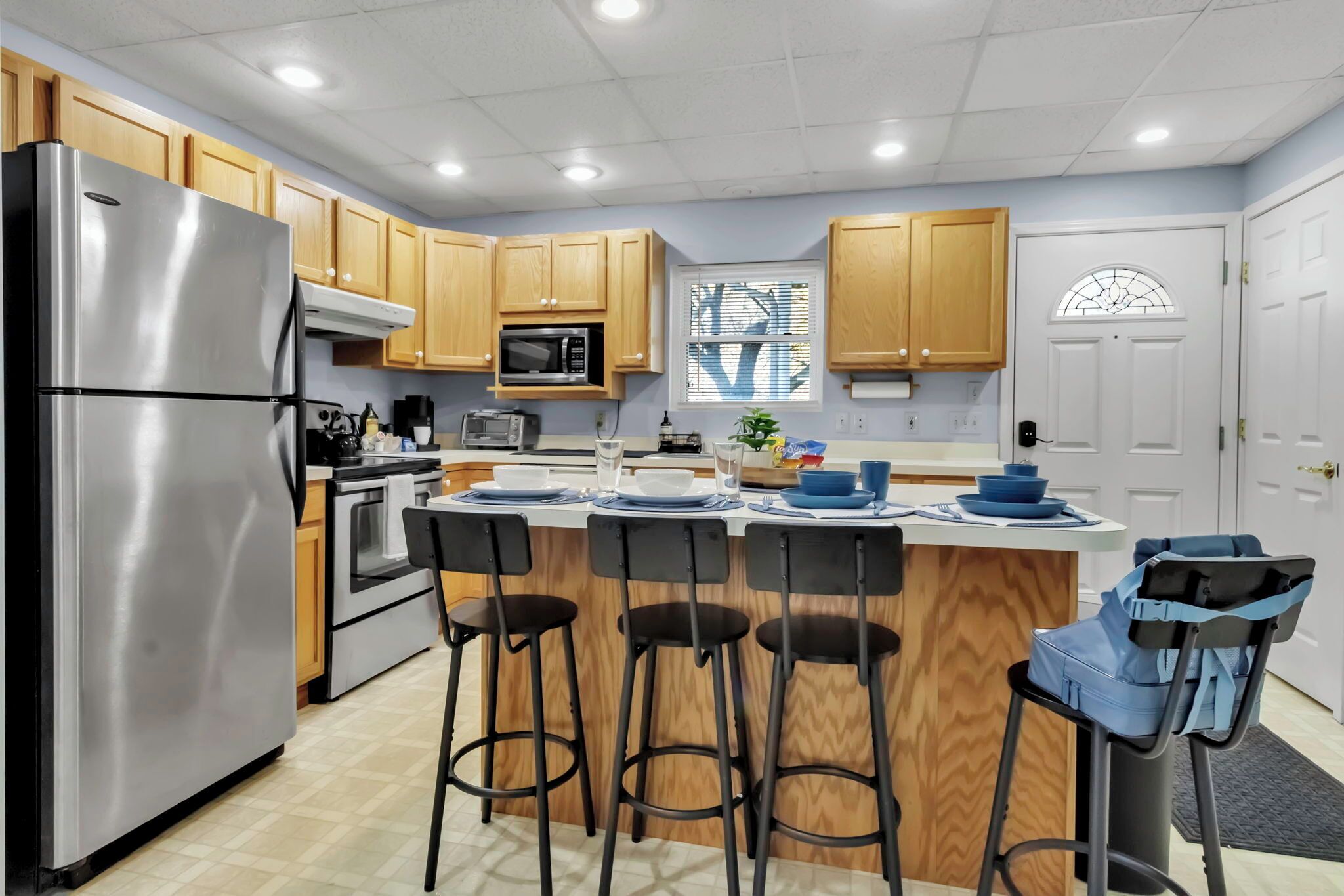 Una cocina moderna con armarios de madera, electrodomésticos de acero inoxidable, una isla central con taburetes y vistas al exterior a través de una ventana.