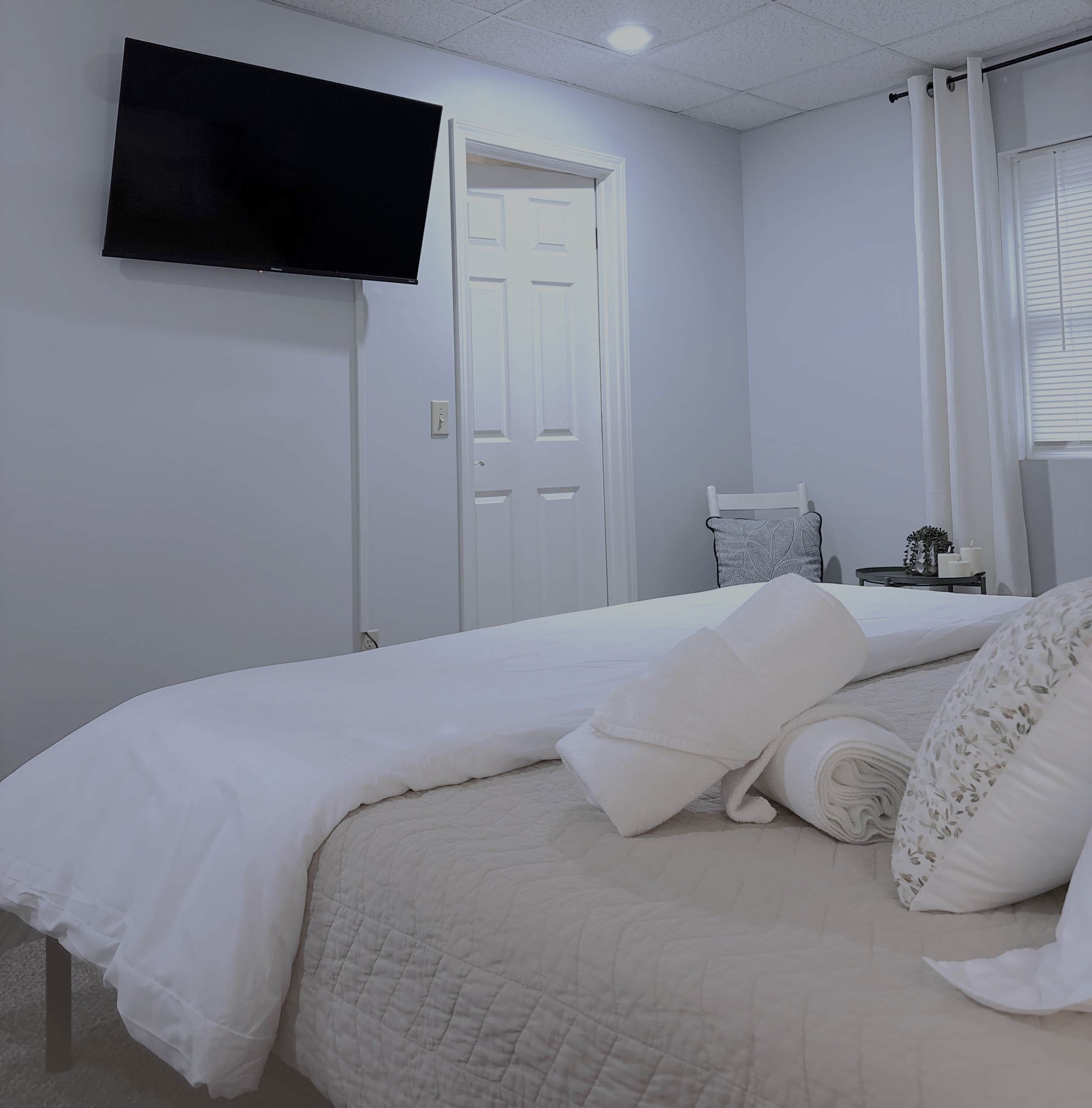 Een slaapkamer met een bed, een aan de muur bevestigde televisie, een deur en een raam met gordijnen.