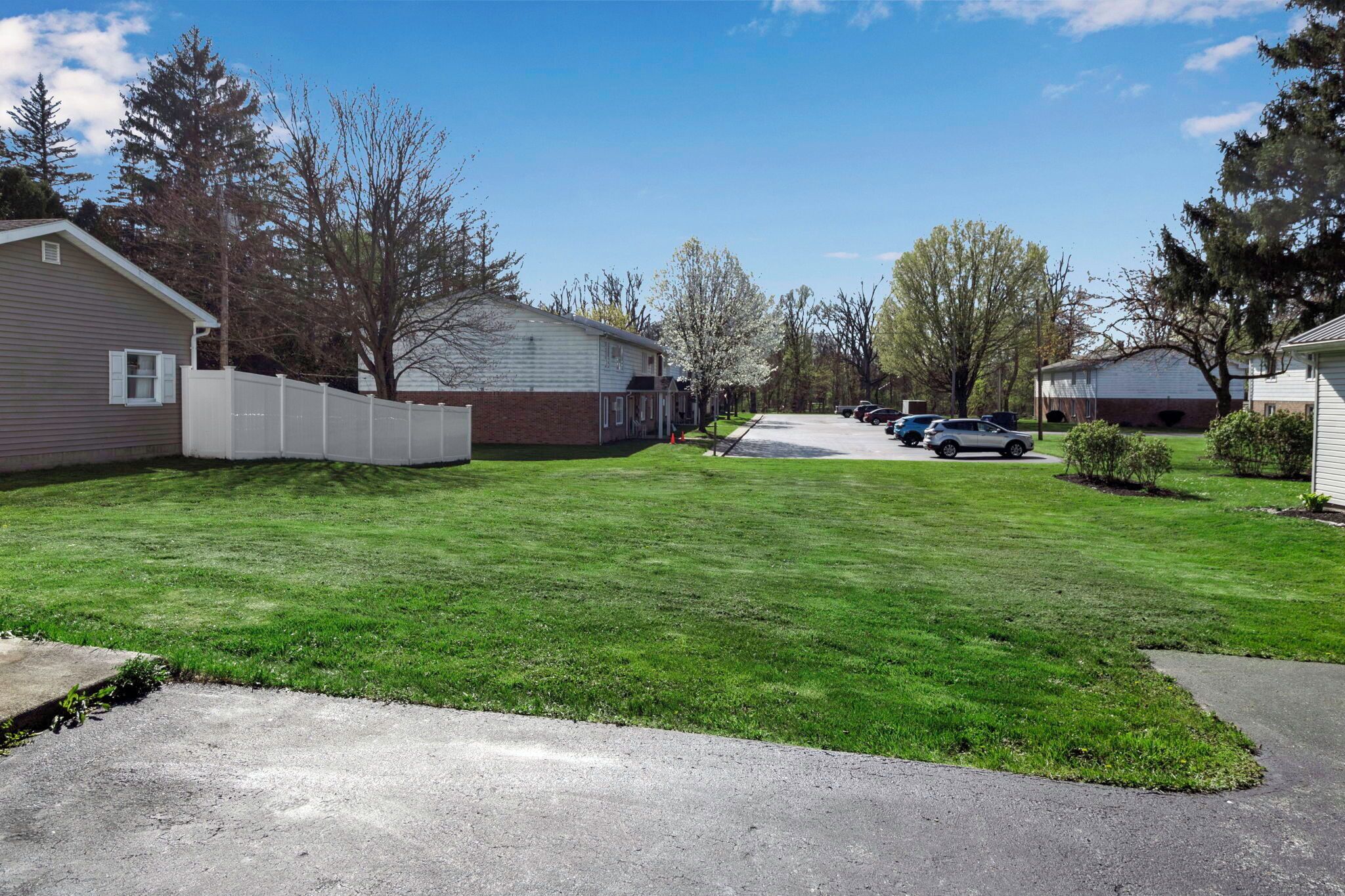 A residential street with houses, a well-maintained lawn, and parked cars.