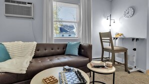 A modern living room with a brown leather sofa, a coffee table with a chess set, and a desk with a chair. - Suite Retreat: Cozy Walkable Akron Village Getaway (Akron)