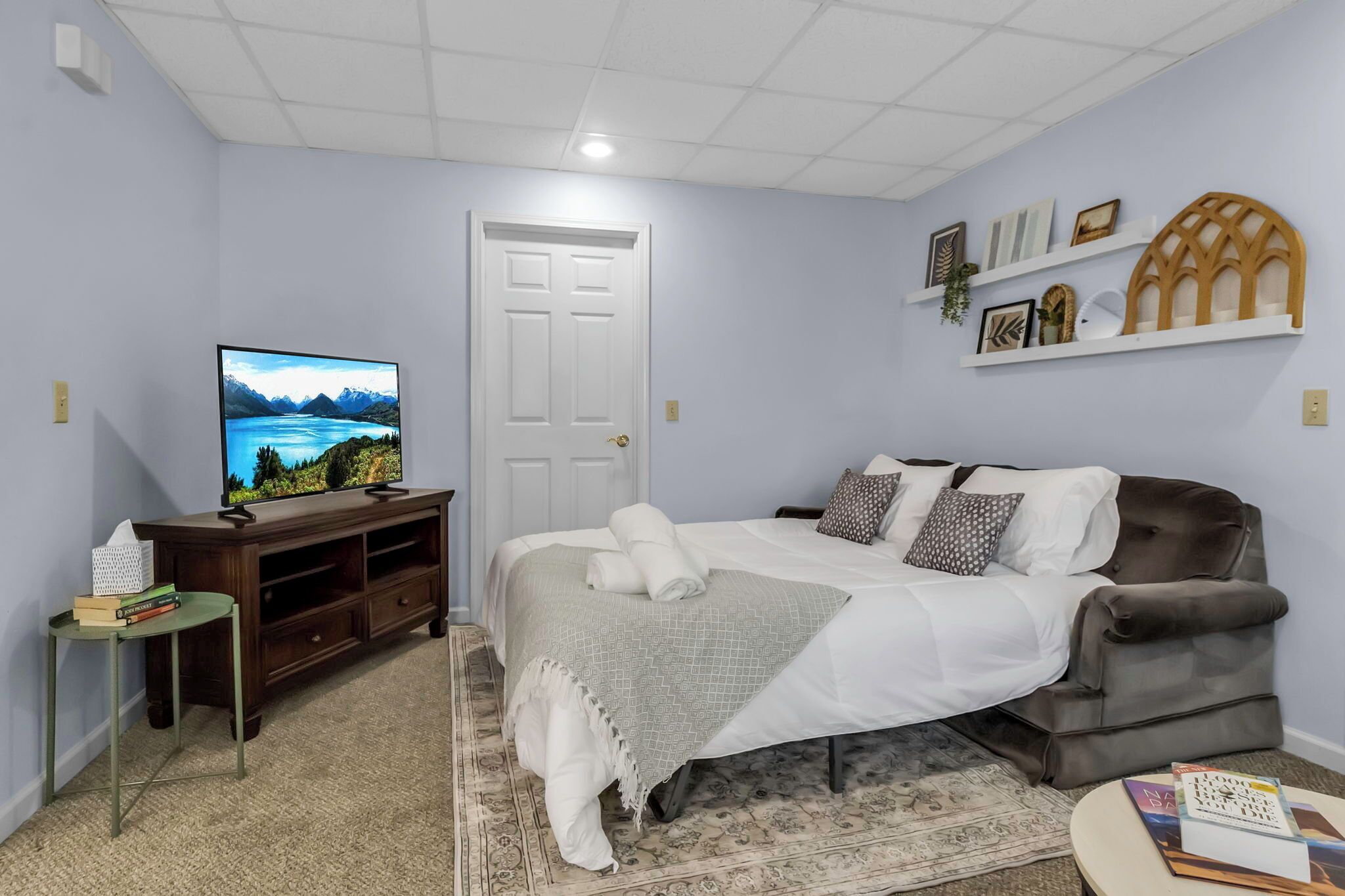 A bedroom with a bed, a television, a desk, and shelves with decorative items.