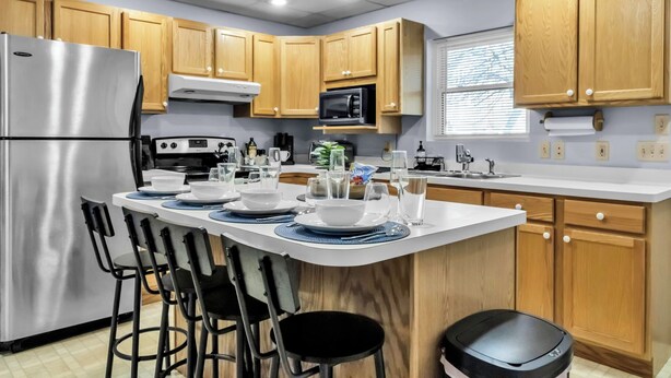 A modern kitchen with wooden cabinets, stainless steel appliances, and a central island with bar stools. - Suite Retreat: Cozy Walkable Akron Village Getaway (Akron)