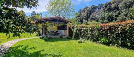 Ein kleines Haus mit Terrasse, umgeben von üppiger Vegetation und blauem Himmel.