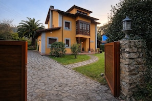 A two-story house with a stone pathway leading to the entrance, surrounded by greenery and a stone wall.