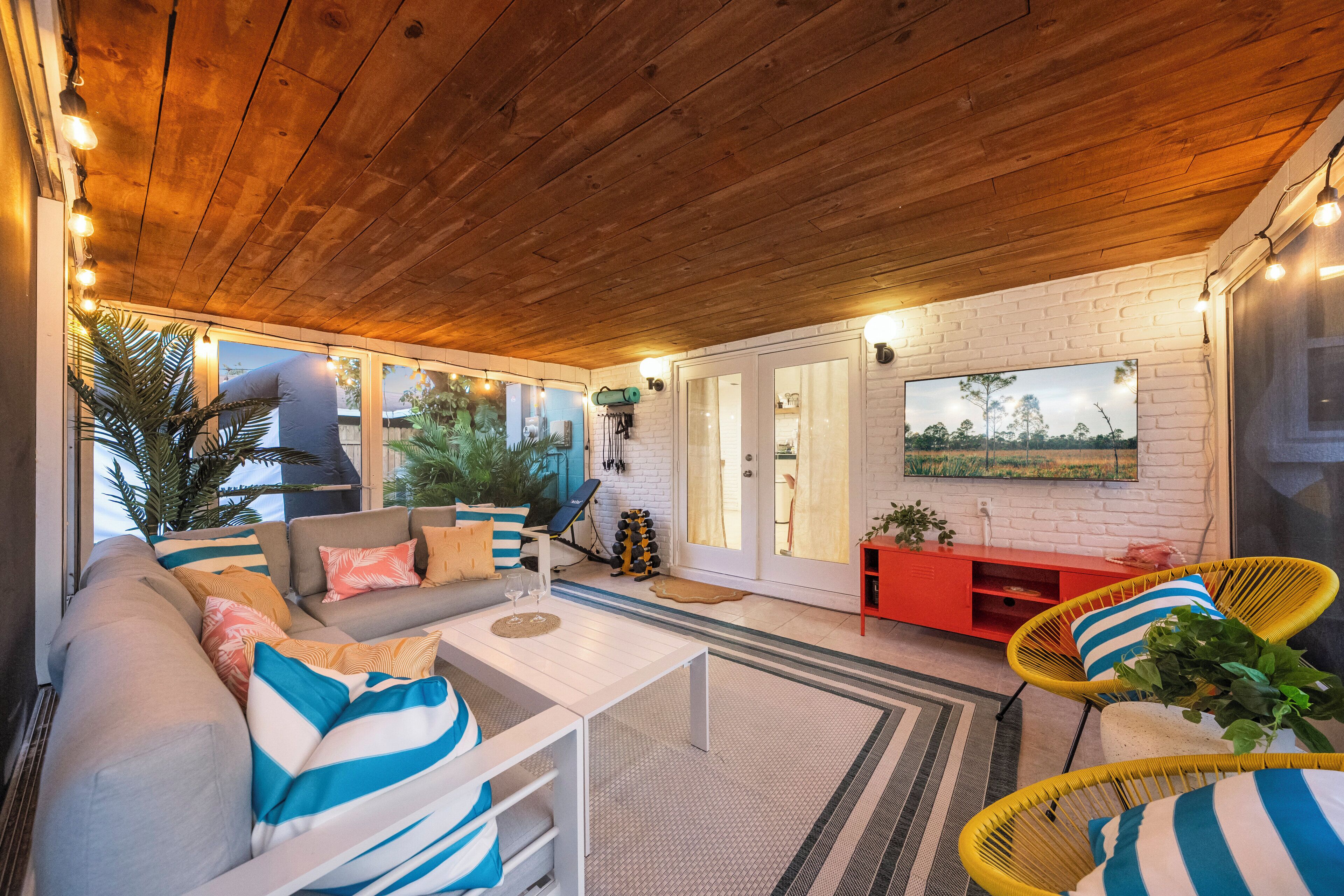 Un salon chaleureux avec un plafond en bois, un ensemble de canapés, une table basse et un meuble de rangement rouge pour les appareils multimédias.