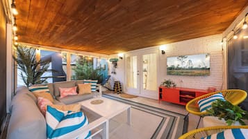 Un salon chaleureux avec un plafond en bois, un ensemble de canapés, une table basse et un meuble de rangement rouge pour les appareils multimédias.