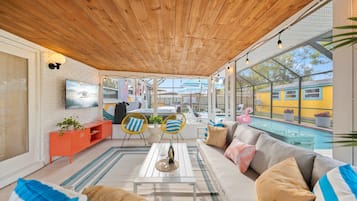 Un salon moderne avec un plafond en bois, une piscine et un téléviseur fixé à un mur en briques.