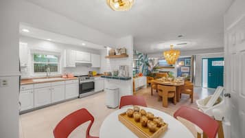 Une cuisine moderne avec des meubles blancs, un coin repas avec des chaises rouges et un îlot central sur lequel se trouve un plateau de muffins.