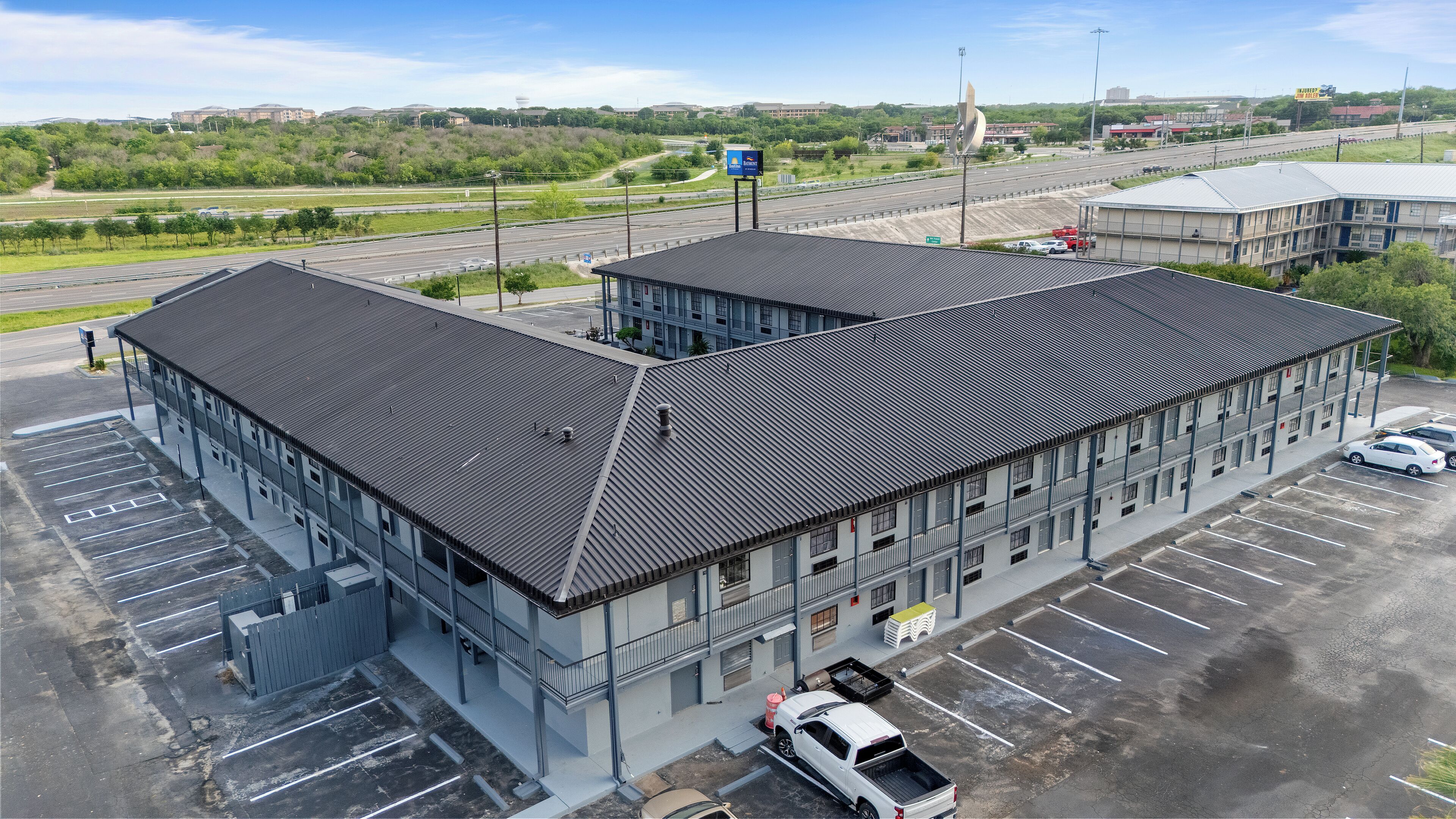 A multi-story building with a flat roof, parking lot, and a view of a highway.