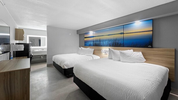 A modern hotel room with two beds, a wooden headboard, a large wall-mounted artwork, and a kitchenette area. - Days Inn By Wyndham San Antonio Near Lackland Afb (San Antonio)