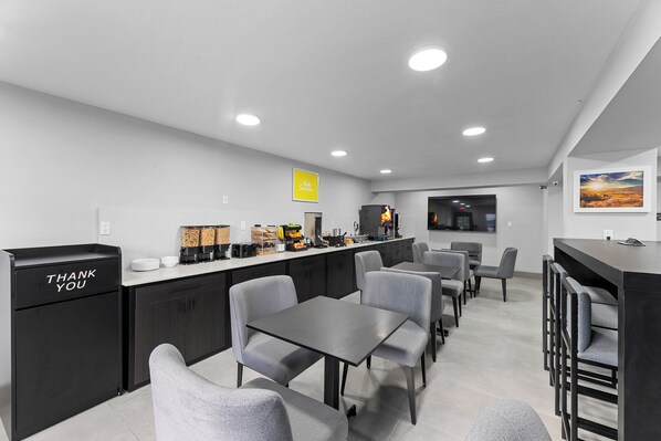 A modern kitchen with a black refrigerator, a coffee station, and a dining area with grey chairs and tables.