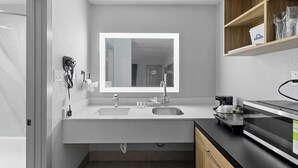 A modern kitchen with a double sink, a microwave, and a wooden shelf above the counter. - Days Inn By Wyndham San Antonio Near Lackland Afb (San Antonio)