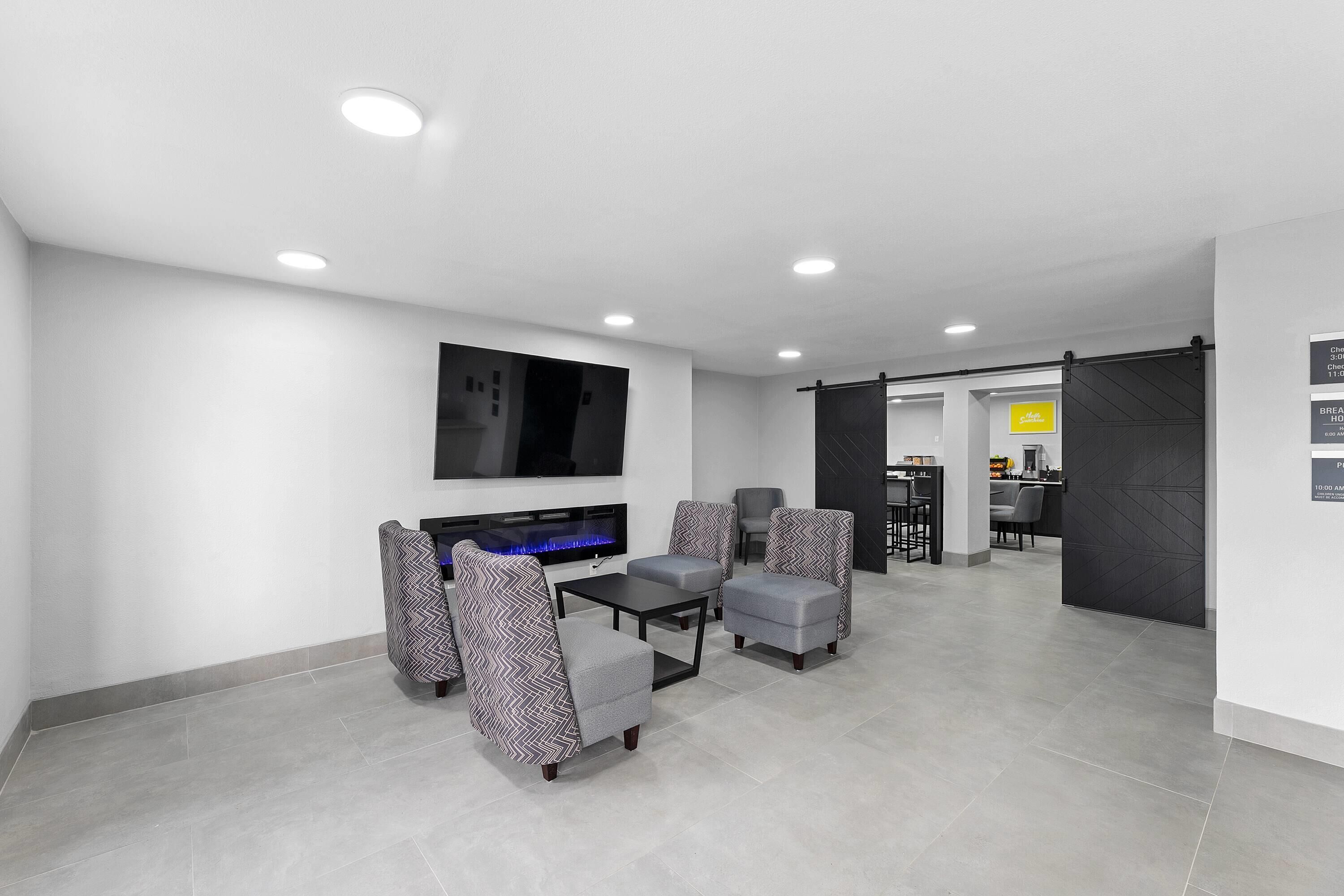 A modern living room with a flat-screen TV, grey patterned armchairs, a coffee table, and a fireplace.