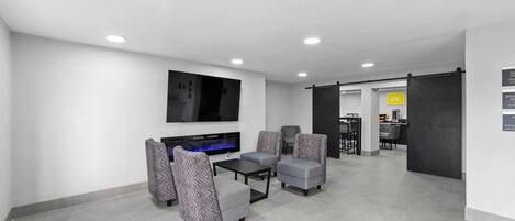 A modern living room with a flat-screen TV, grey patterned armchairs, a coffee table, and a fireplace.