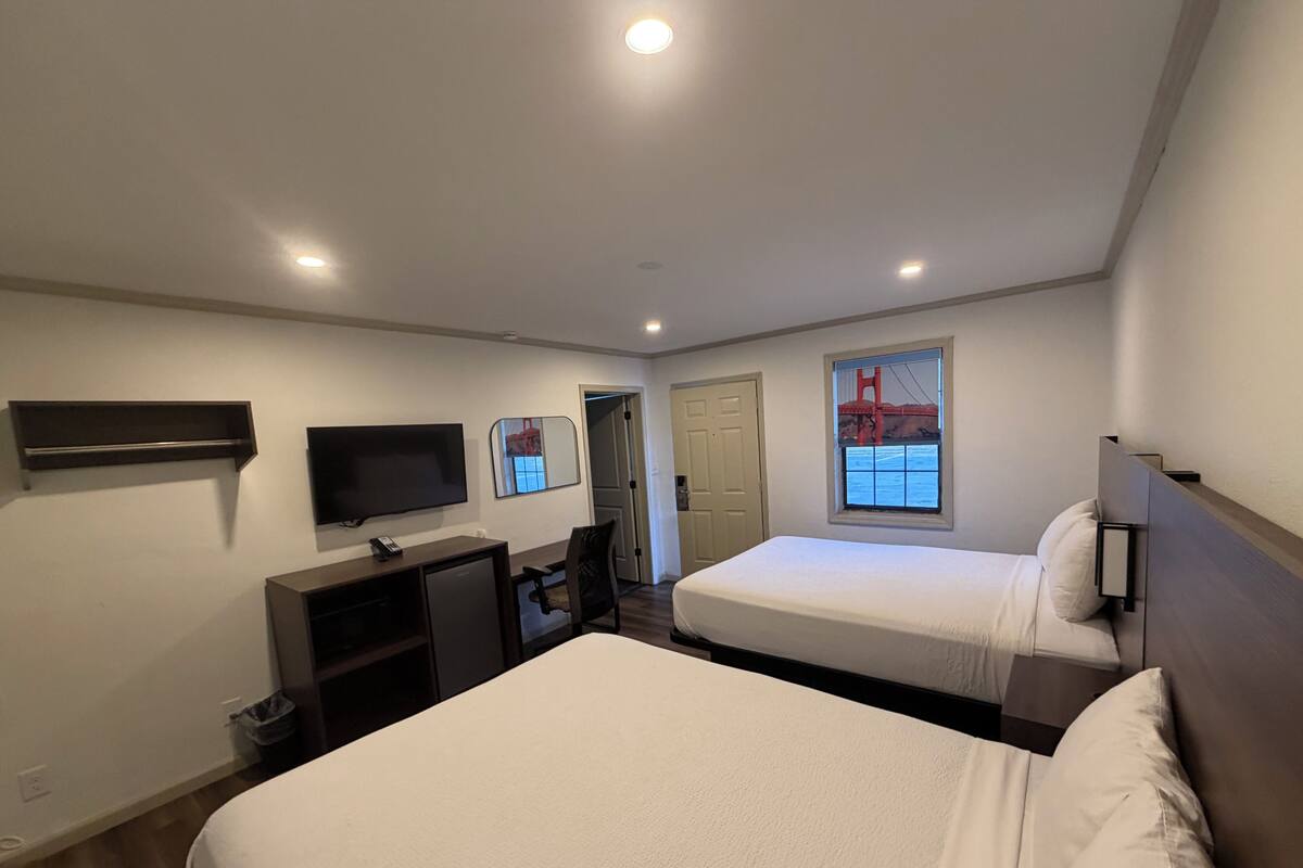 Habitación de hotel con dos camas, un televisor, un escritorio y una ventana con vistas al Puente Golden Gate.