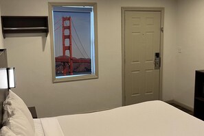 Une chambre à coucher avec un lit, une porte, une étagère fixée au mur et une fenêtre donnant sur le pont du Golden Gate.