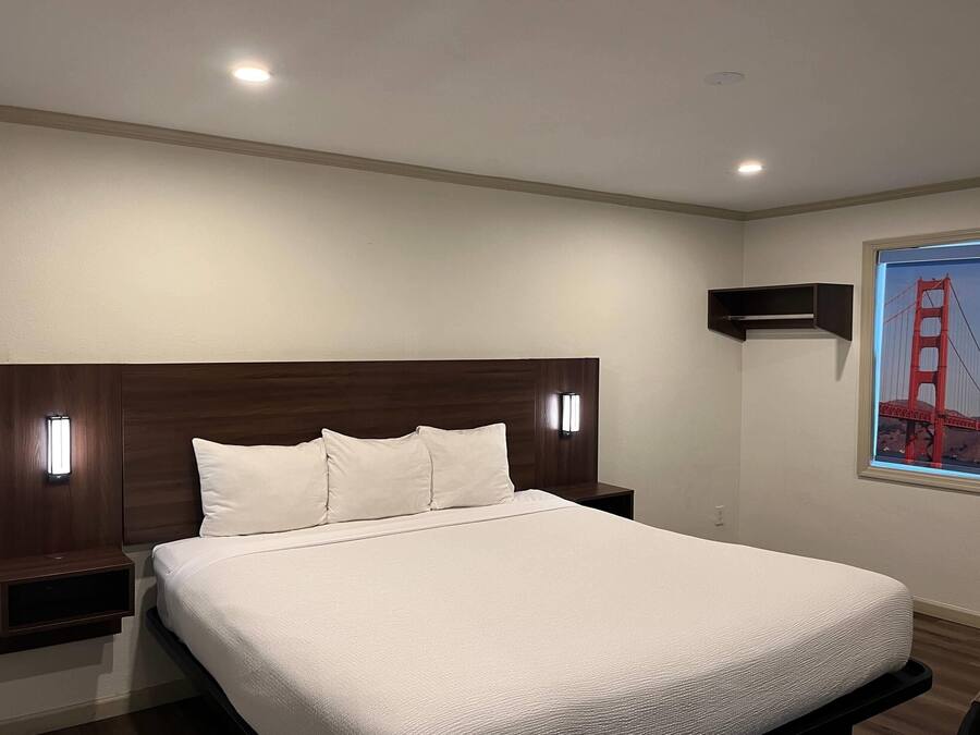 A neatly made bed with a wooden headboard, two bedside tables with lamps, and a window with a view of the Golden Gate Bridge.