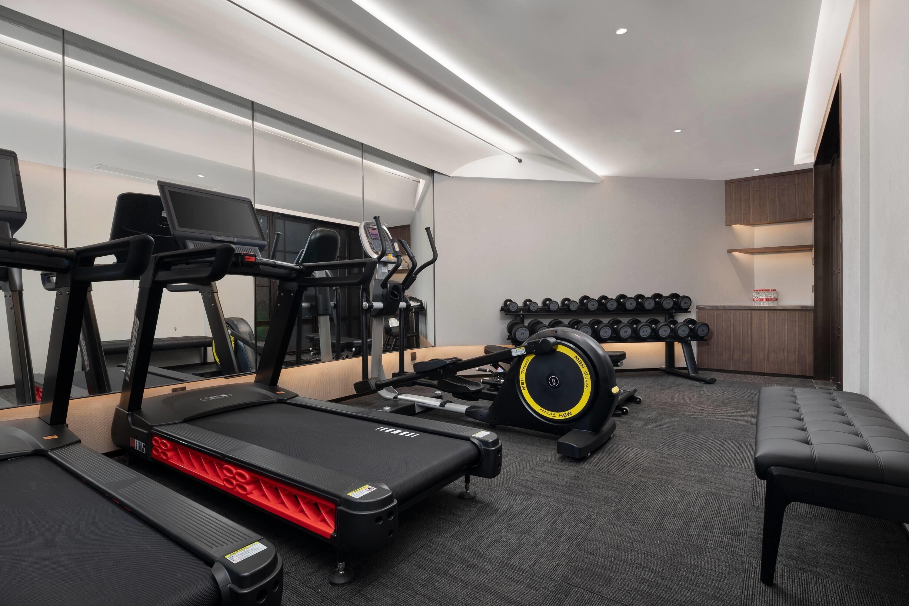 A modern gym with treadmills, a rowing machine, and a bench.