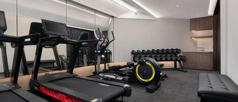 A modern gym with treadmills, a rowing machine, and a bench.