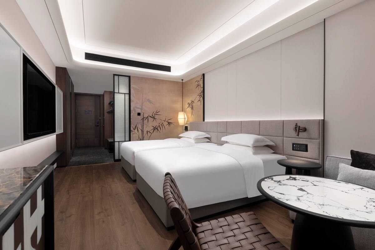 Quarto de hotel moderno com uma cama grande, uma mesa redonda pequena, um sofá e uma televisão.