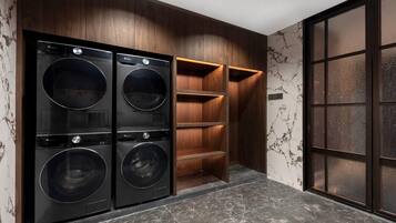 A laundry room with four black front-loading washers and dryers, wooden shelving, and a marble-patterned wall.