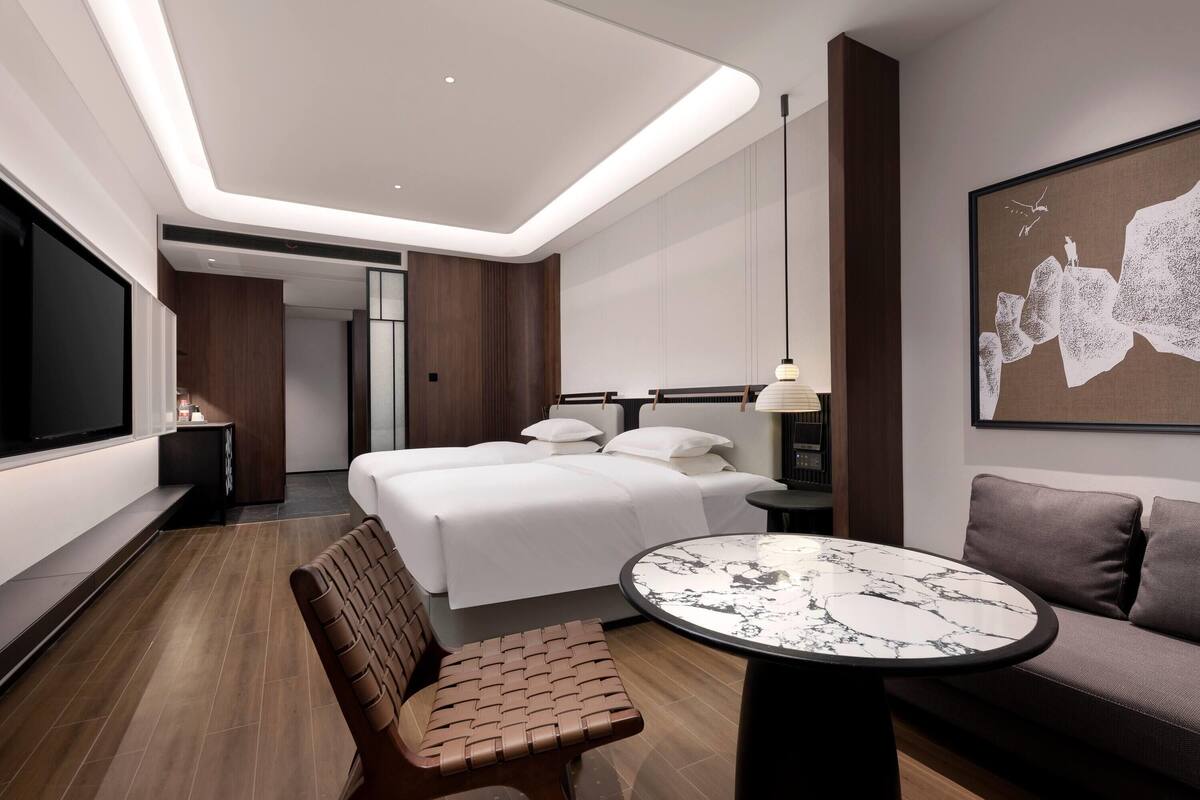 Quarto de hotel moderno com cama, mesa redonda, sofá e televisão.