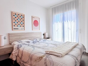 Ein modernes Schlafzimmer mit einem Bett, einem Nachttisch, einer Lampe und zwei gerahmten Kunstwerken an der Wand.
