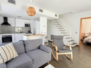 Eine moderne Wohnung mit Küche, einem grauen Sofa, einem Holzstuhl und einer Treppe.