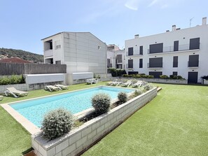 Un edificio moderno con piscina, sillas de descanso y un césped cuidado.