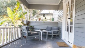 A covered porch with a gray sofa, two chairs, and a small table. There are potted plants and a wooden bench.