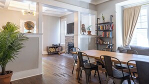 A spacious living area with a wooden dining table, chairs, a bookshelf, and a television.