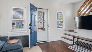 Uma sala de estar moderna com uma porta azul, escada de madeira e televisão de tela plana.