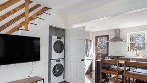 Cozinha moderna com televisão grande, máquina de lavar e secar integradas, escada de madeira e vista para o exterior.