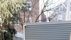 A backyard with artificial grass, a white patio chair, and a shed. - Charming 2-bedroom apartment with AC, WiFi in peaceful Ventnor City (Ventnor City)