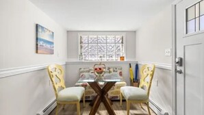 A dining area with a glass-top table, two chairs, a window with frosted glass, and a painting on the wall. - Charming 2-bedroom apartment with AC, WiFi in peaceful Ventnor City (Ventnor City)