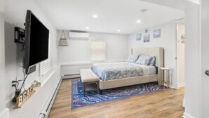 A bedroom with a bed, a TV, a bench, and a patterned rug. - Charming 2-bedroom apartment with AC, WiFi in peaceful Ventnor City (Ventnor City)