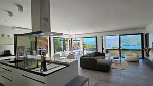 A modern kitchen with a central island, large windows offering a view of the sea, and a living area with a sofa and a coffee table. - Villa Haut Standing Stella Di Mare panoramic view (Propriano)