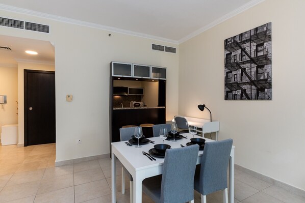 A dining area with a white table set for four, a kitchen area with cabinets and a microwave, and a black and white artwork on the wall.