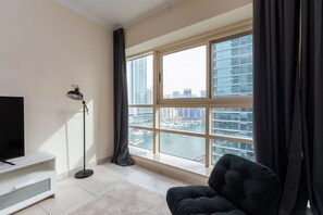 Een moderne woonkamer met een groot raam, een flatscreen televisie, een vloerlamp en een donkere bank.