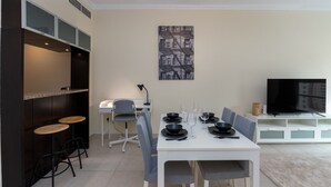 Un espace repas moderne avec une table blanche dressée pour quatre personnes, des chaises grises et un tableau abstrait en noir et blanc accroché au mur.