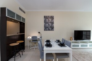 Un comedor moderno con una mesa blanca para cuatro, sillas grises y un cuadro abstracto blanco y negro en la pared.