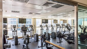 Une salle de sport équipée de divers appareils d’exercice, dotée de grandes fenêtres et d’un mur recouvert de miroirs.