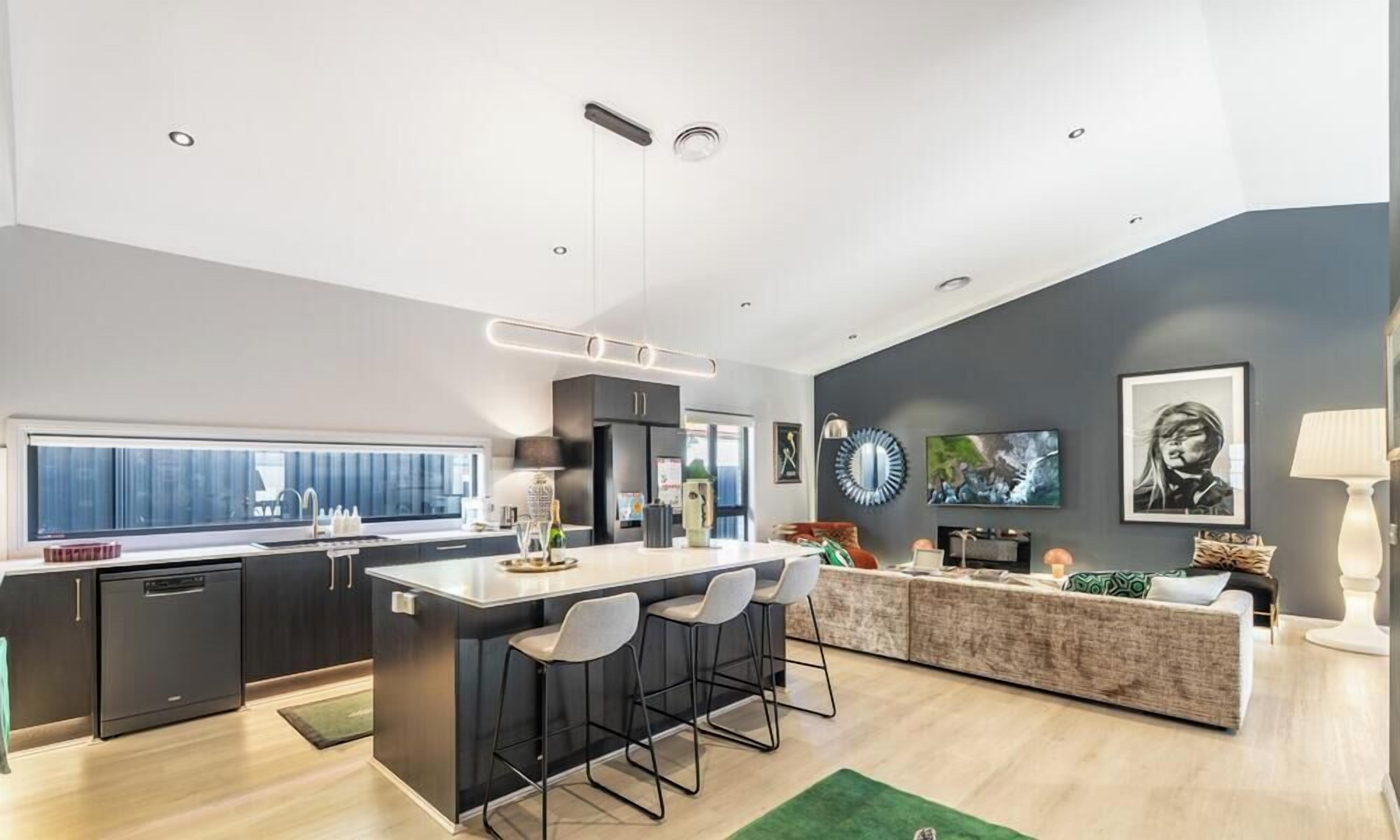 A modern kitchen with a central island, bar stools, and a dining area with a sofa and coffee table.