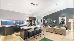 Una cocina moderna con una isla central, taburetes de bar y un comedor con sofá y mesa de centro.