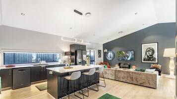 A modern kitchen with a central island, bar stools, and a dining area with a sofa and coffee table.